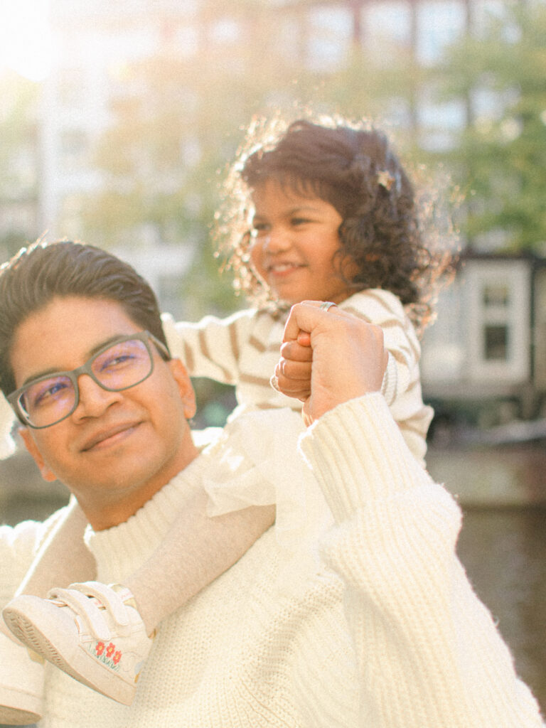 Toddler sits on father's shoulders with the sun behind them.
