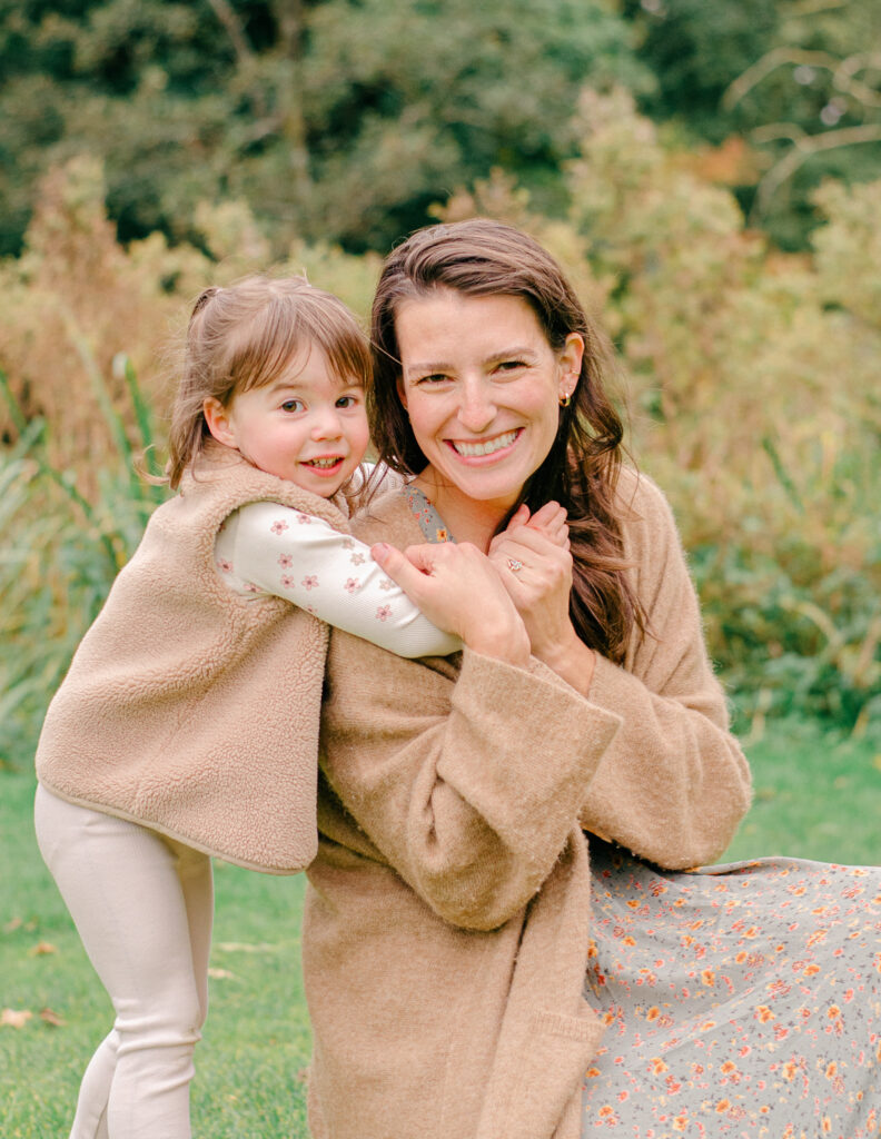 Daughter hugs mom under the fall leaves.
