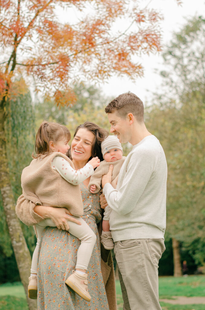 Light-filled image of family of four playing under the fall leaves.