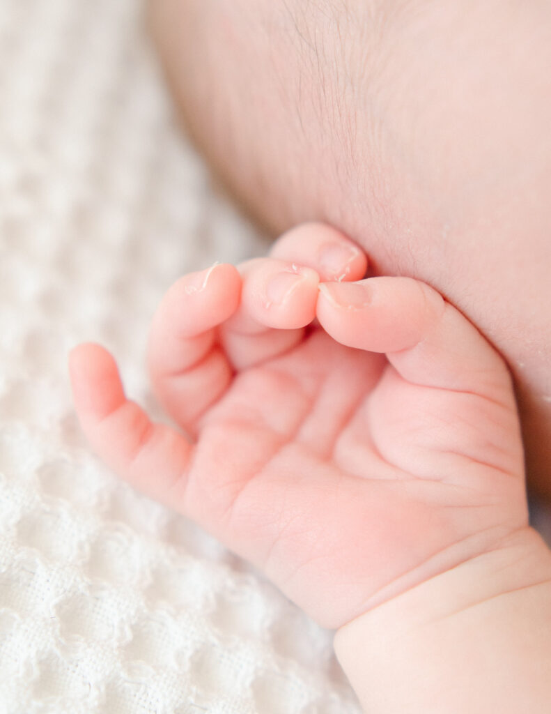 Neutral light detail shot of baby's hand on a white blanket.