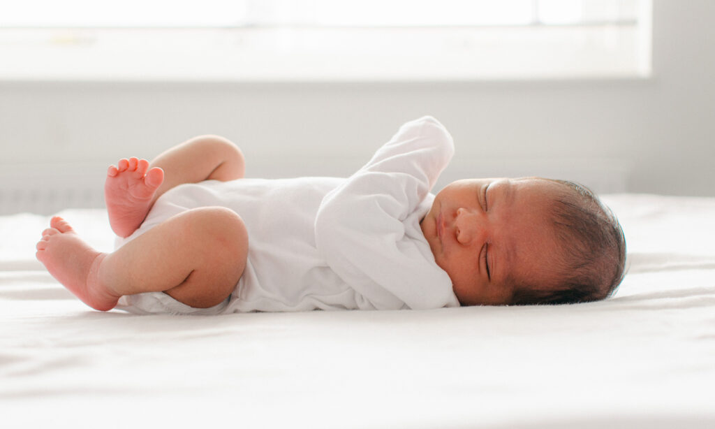 Baby sleeps on bed near a bright window.
