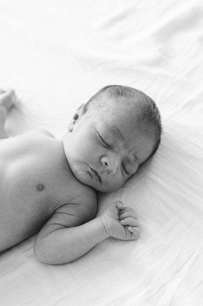 Black and white image of baby sleeping on a bed during home newborn session in Diemen.