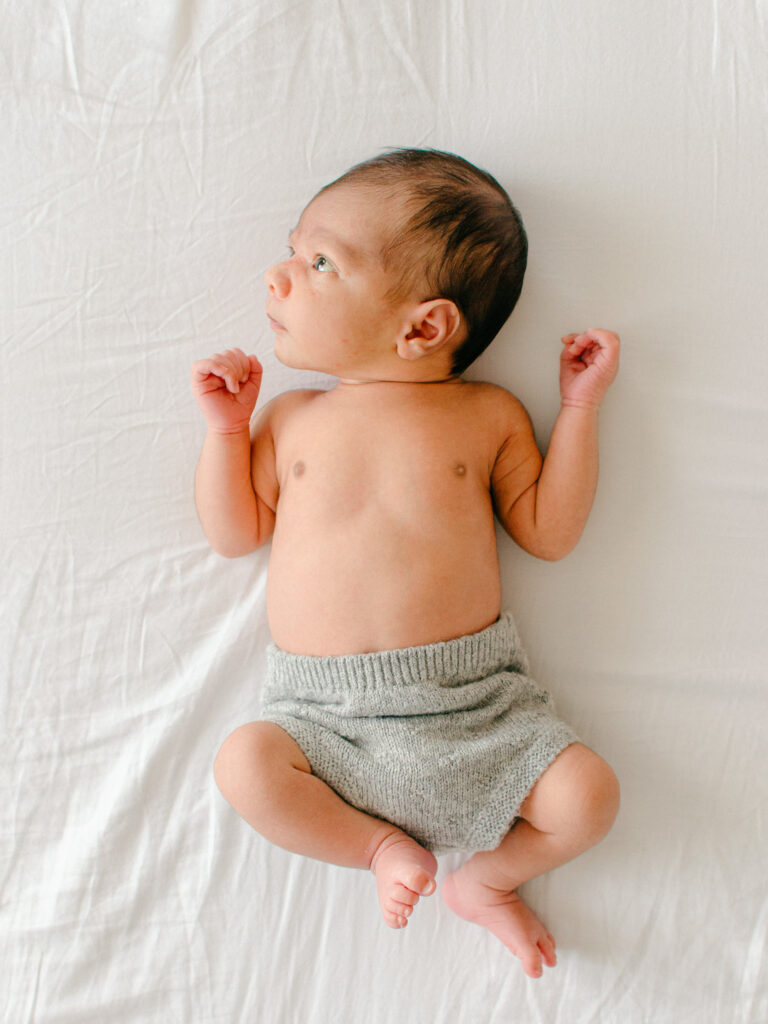 Baby lies on his parents' bed, with his eyes wide open. 