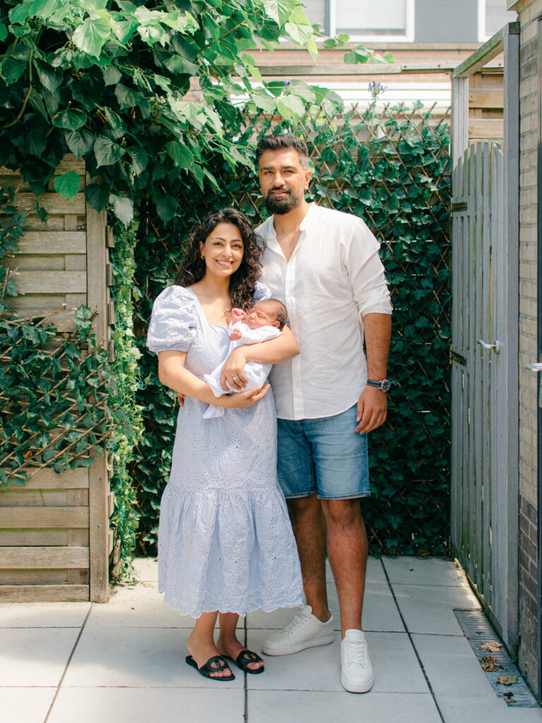 Parents stand with baby boy in their garden. 
