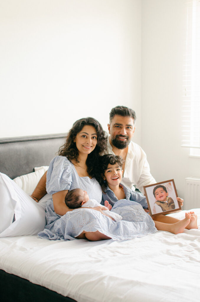 Family sits on the bed together during a newborn photoshoot.