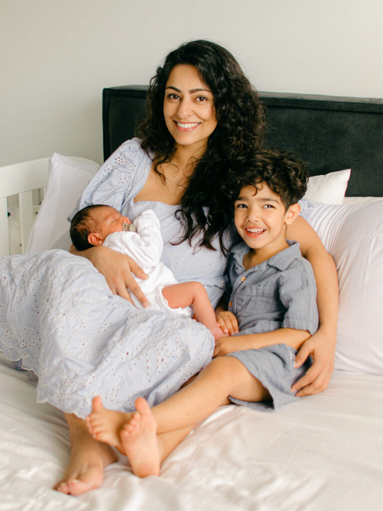 Mom snuggles up with her two boys in the bed during a cozy newborn photoshoot. 