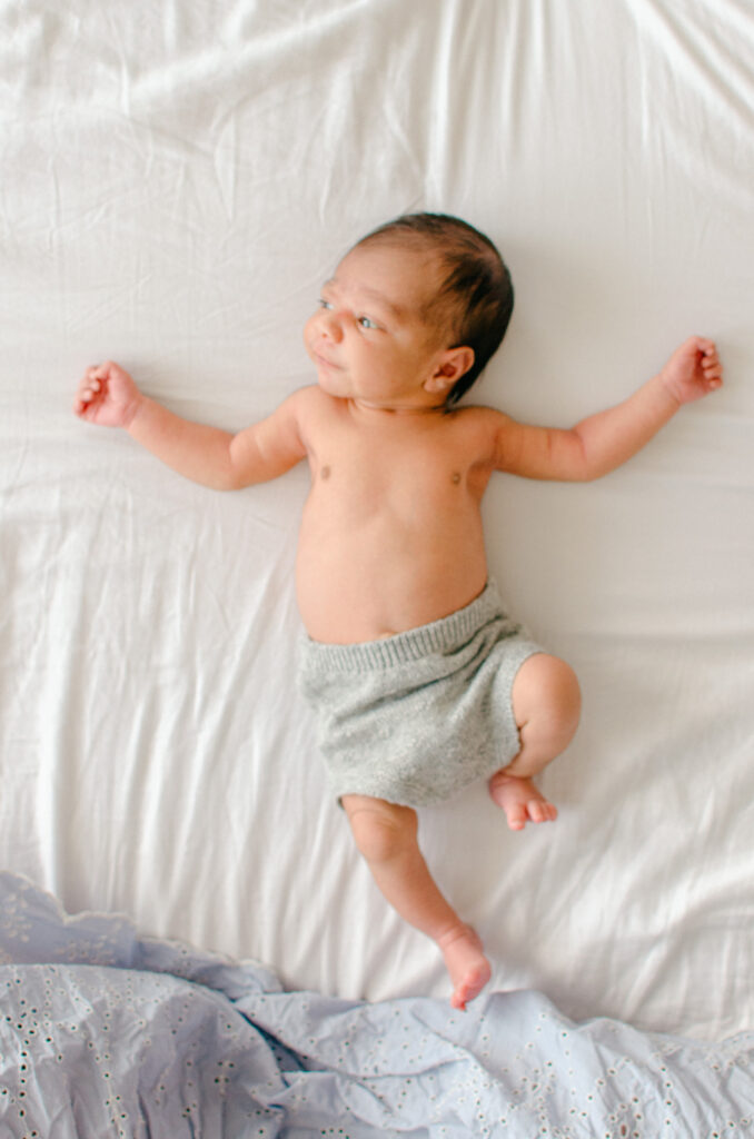 Soft focus portrait of awake baby stretching out his limbs on the bed.