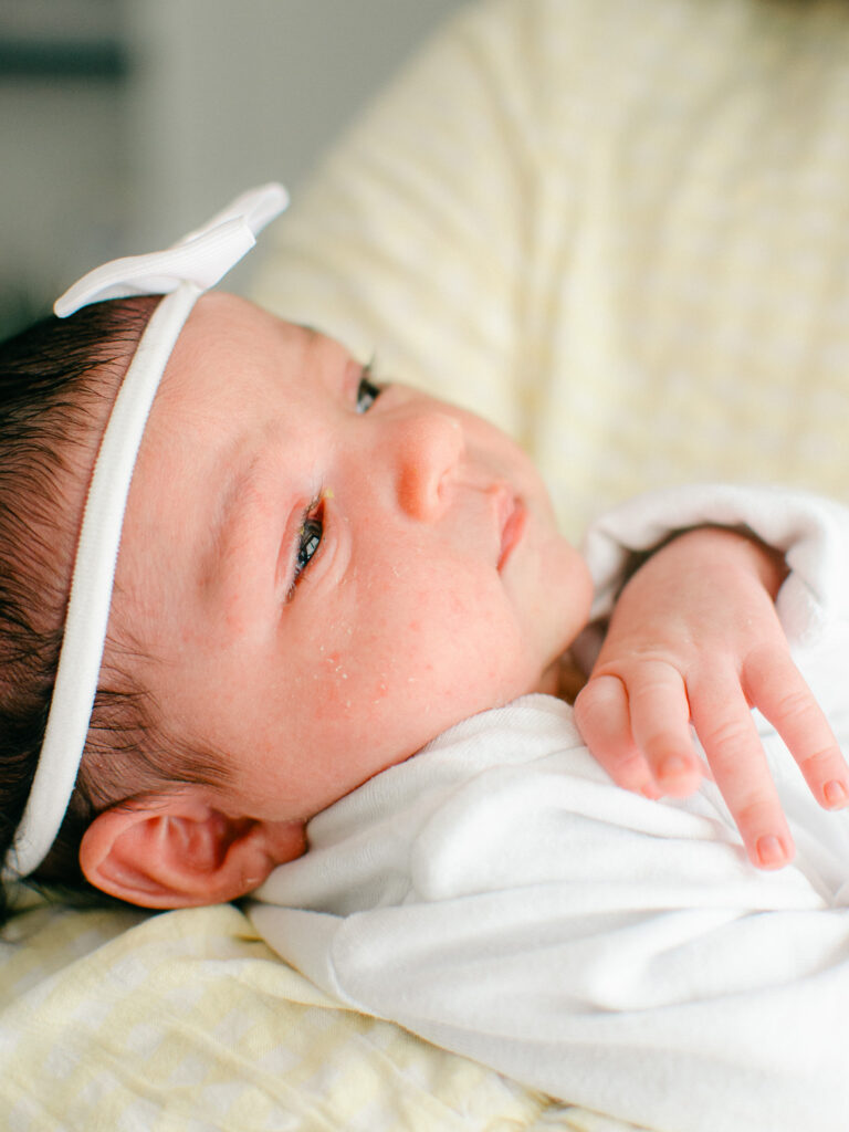 Detail image of a newborn girl in a white onesie and bow.