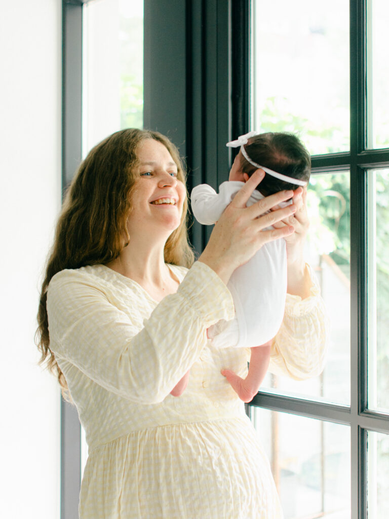 Mom holds newborn baby up in the air during a photoshoot in her home.