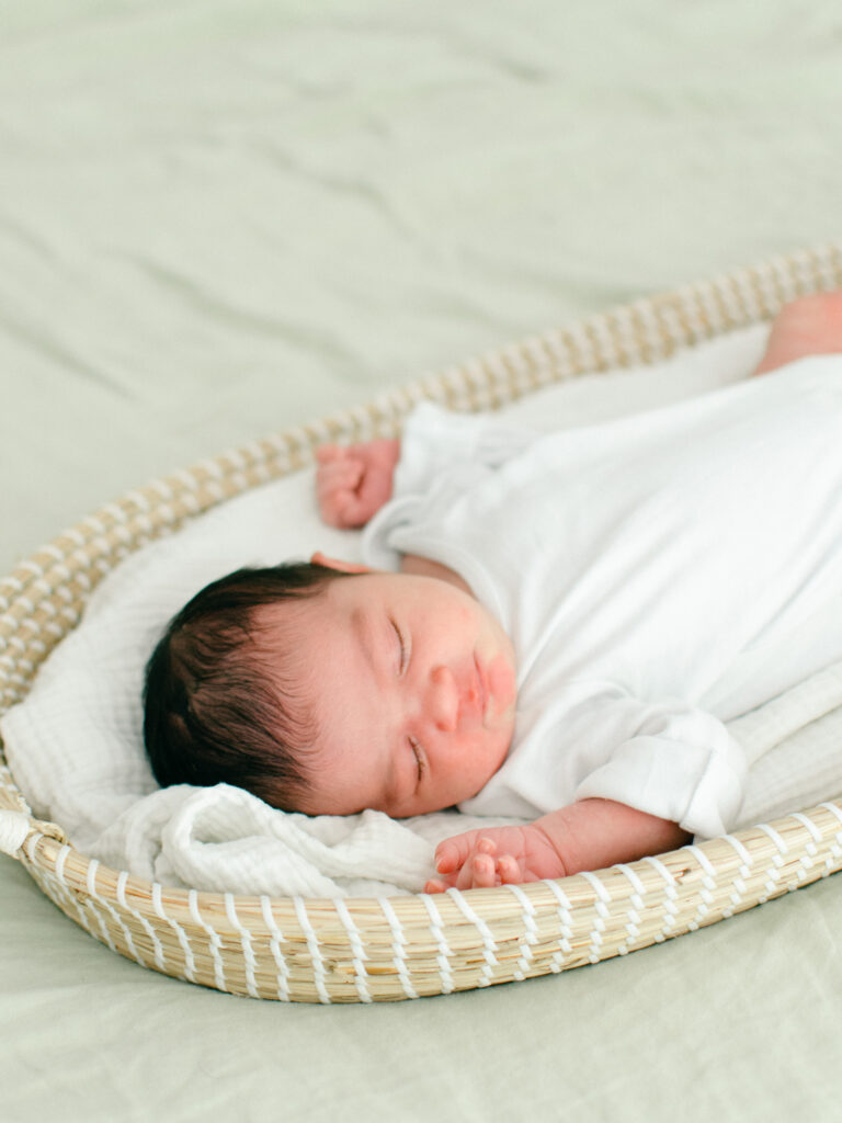 A newborn baby sleeps in a bassinet on her parents' bed.