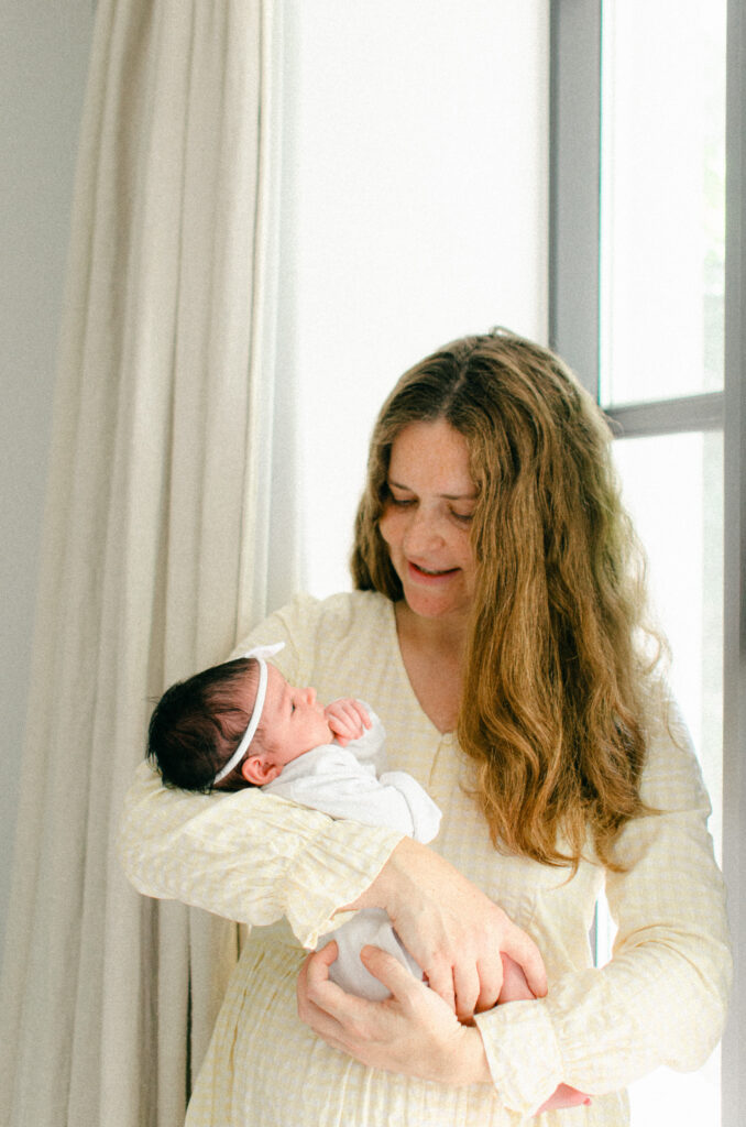 Mother bounces newborn daughter in front of the window.