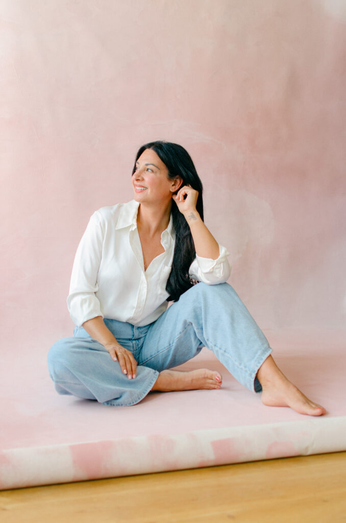 Editorial-style branding photos of a woman entrepreneur on a pink hand-painted canvas in a home photography studio.