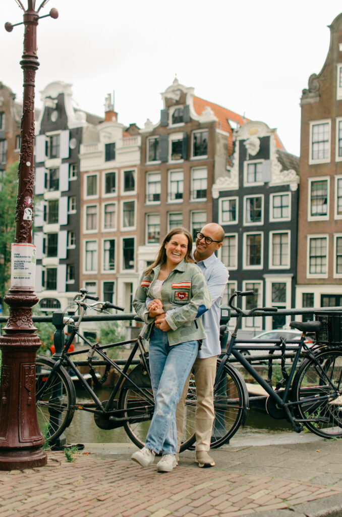 A couple hugs on the Amsterdam Canals with the traditional houses in the background.