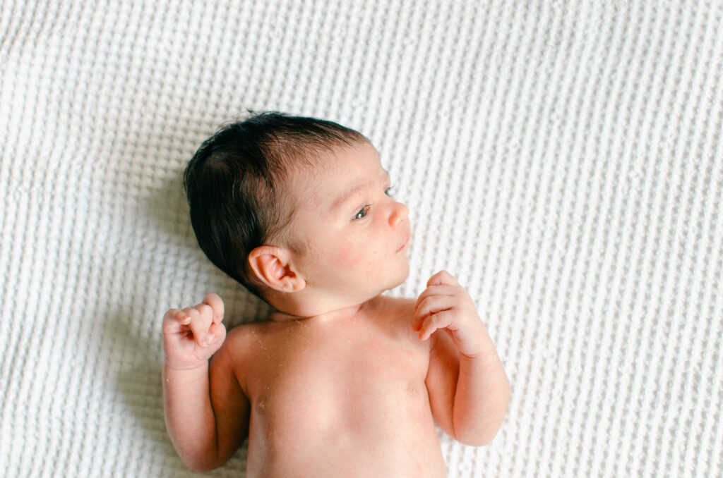 Detail of newborn baby wide awake on a white waffleknit blanket.